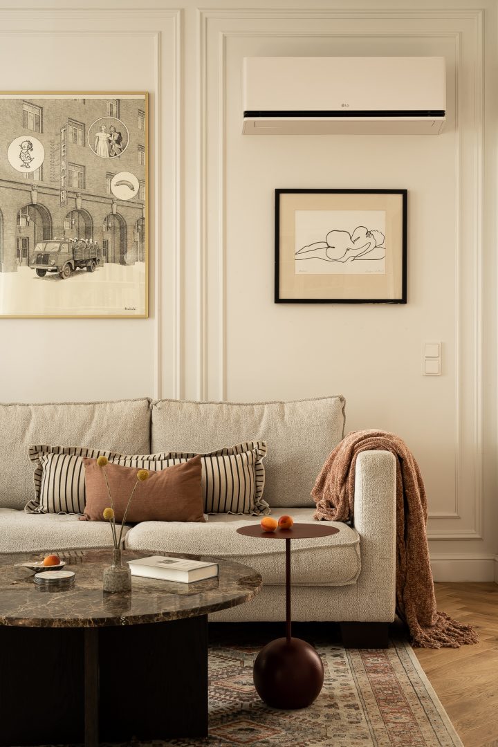 Beżowa sofa z poduszkami, marmurowy stolik i grafiki na ścianie