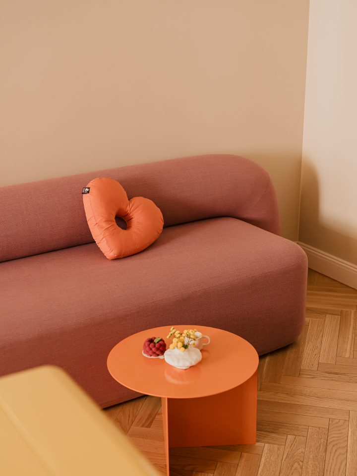 Różowa sofa z poduszką w kształcie serca i pomarańczowy stolik